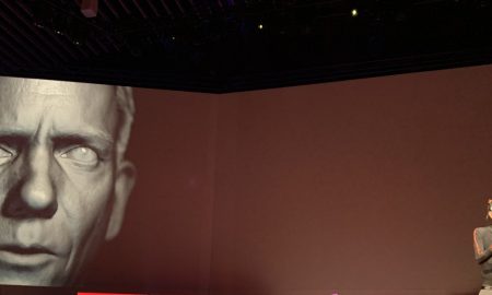 عرض تجريبي لوجه مولد بتقنية الديب فيك على شاشة ضخمة في مؤتمر TED